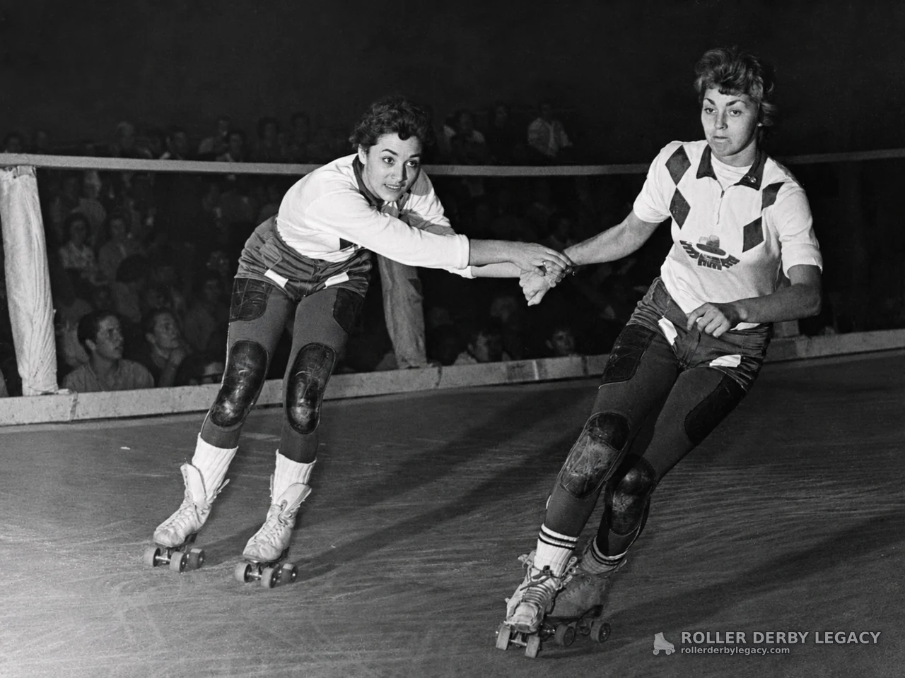 Two Roller Derby Skaters Holding Hands on Indoor Track