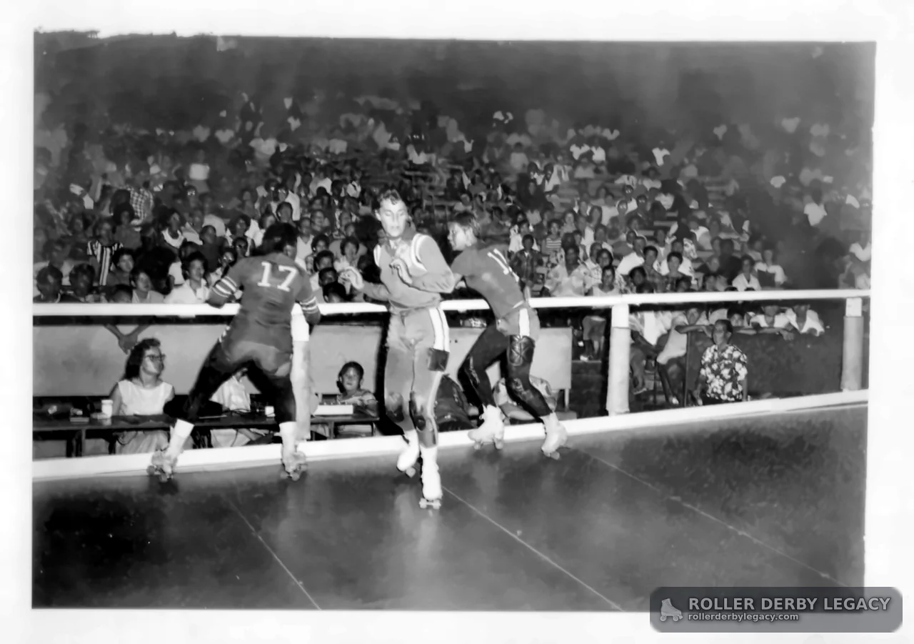 Three Roller Skaters on Indoor Track Before Crowd