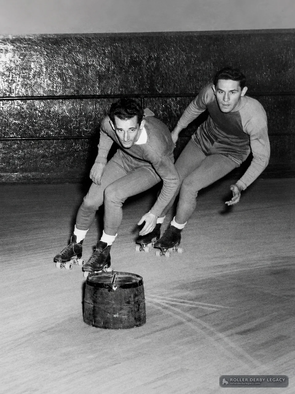 Two Skaters Turning Around a Barrel on an Indoor Rink