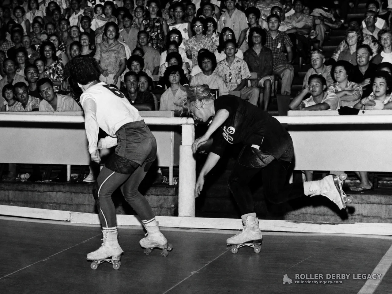 Two Skaters at the Track Rail Before a Packed Crowd