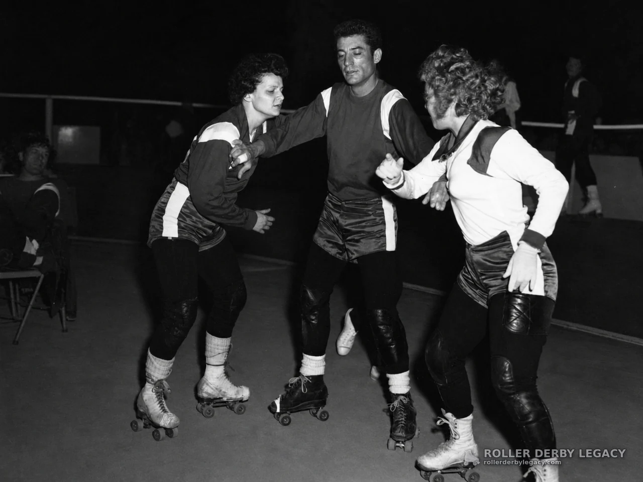 Three Roller Skaters Jostling on an Indoor Track