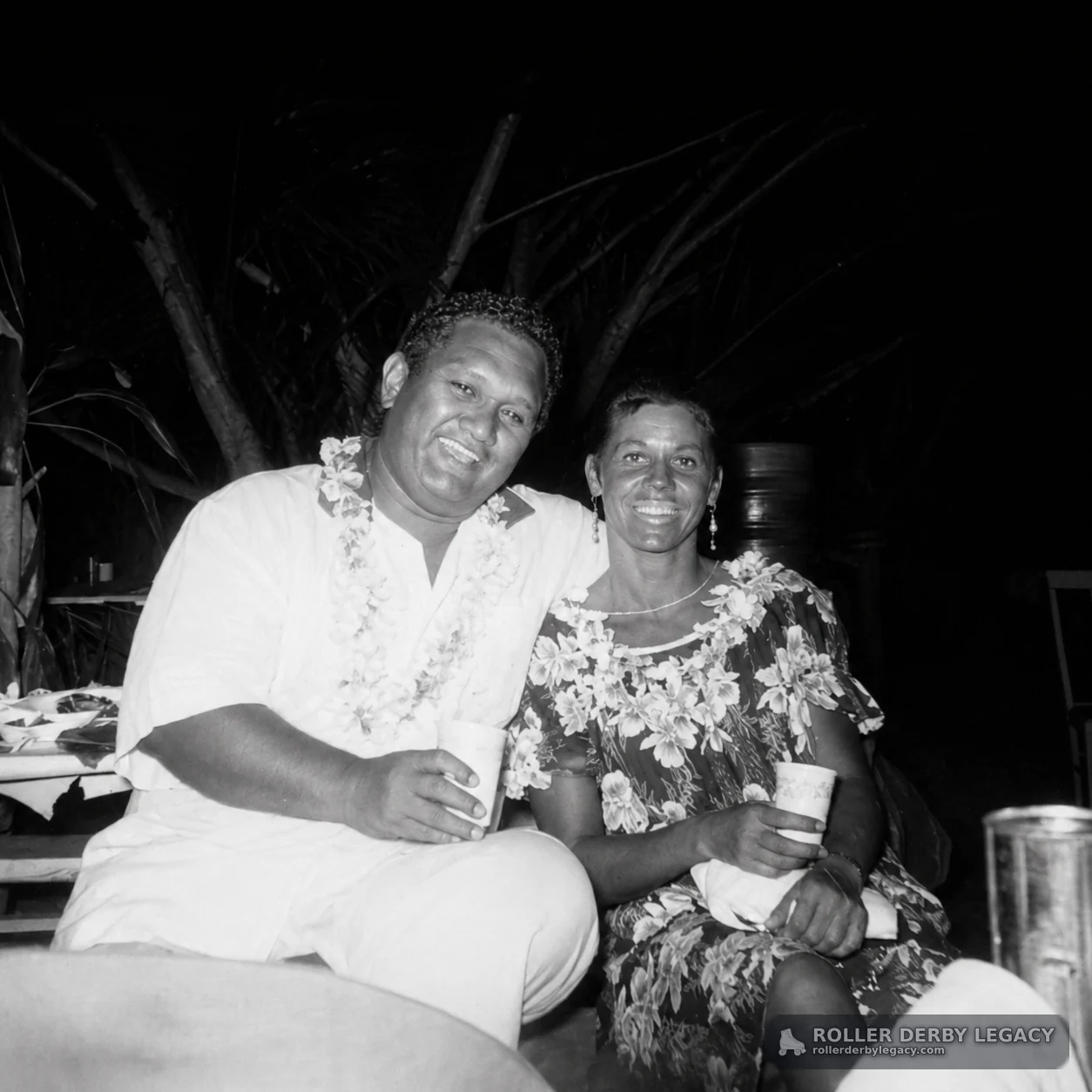 Two Adults Wearing Floral Leis at an Outdoor Night Gathering