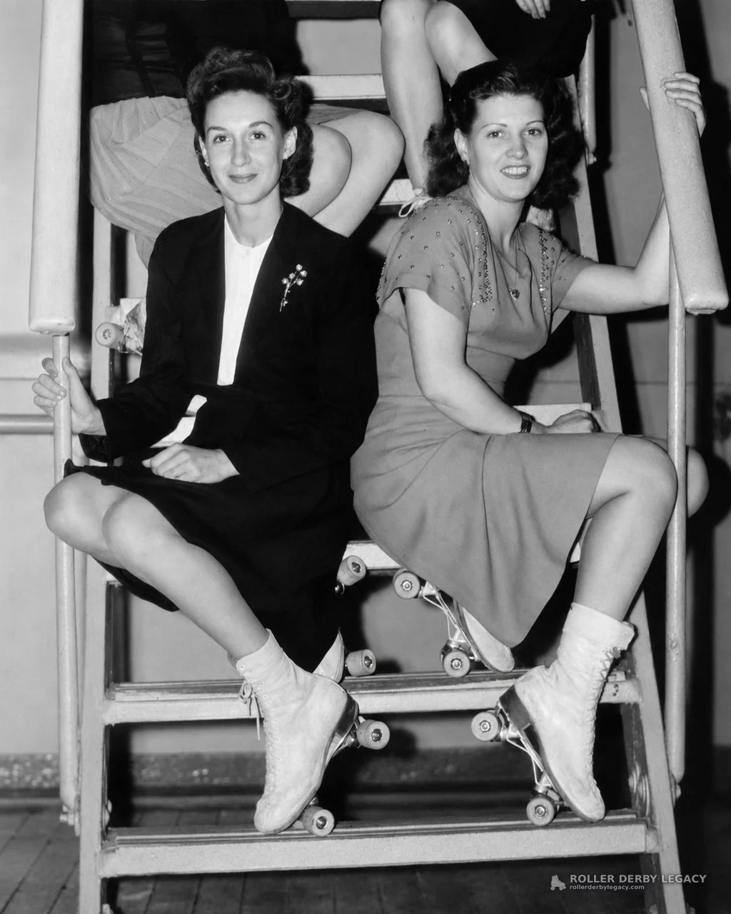 Two Women in Roller Skates Seated on Indoor Stairs