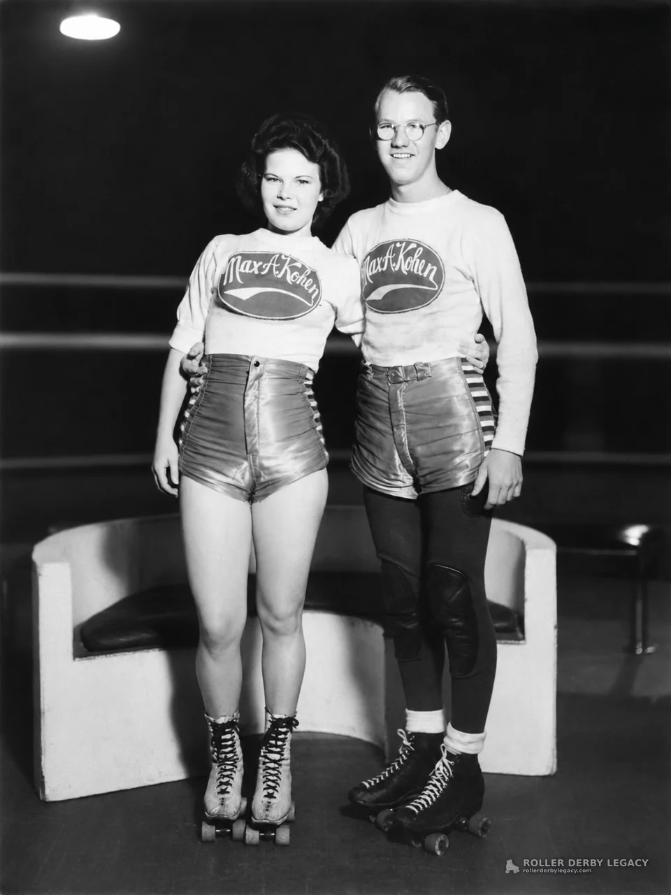 Two Skaters in Max A Kohen Uniforms at an Indoor Rink