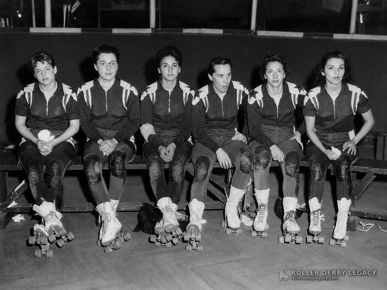 Six Uniformed Roller Skaters Seated on an Indoor Rink Bench