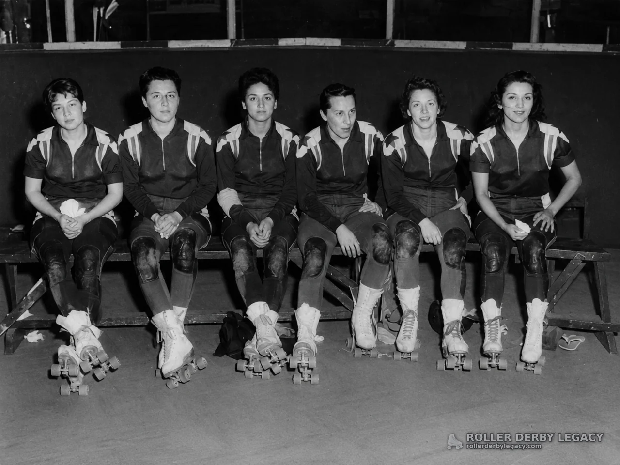 Six Uniformed Roller Skaters Seated on a Rink Bench