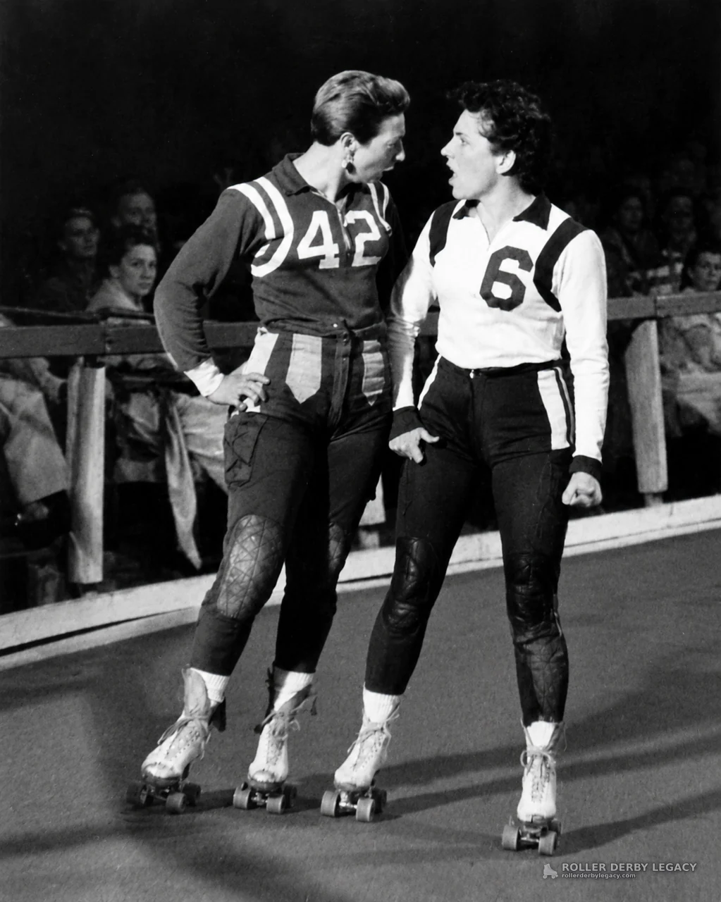 Two Numbered Roller Derby Skaters at an Indoor Rink