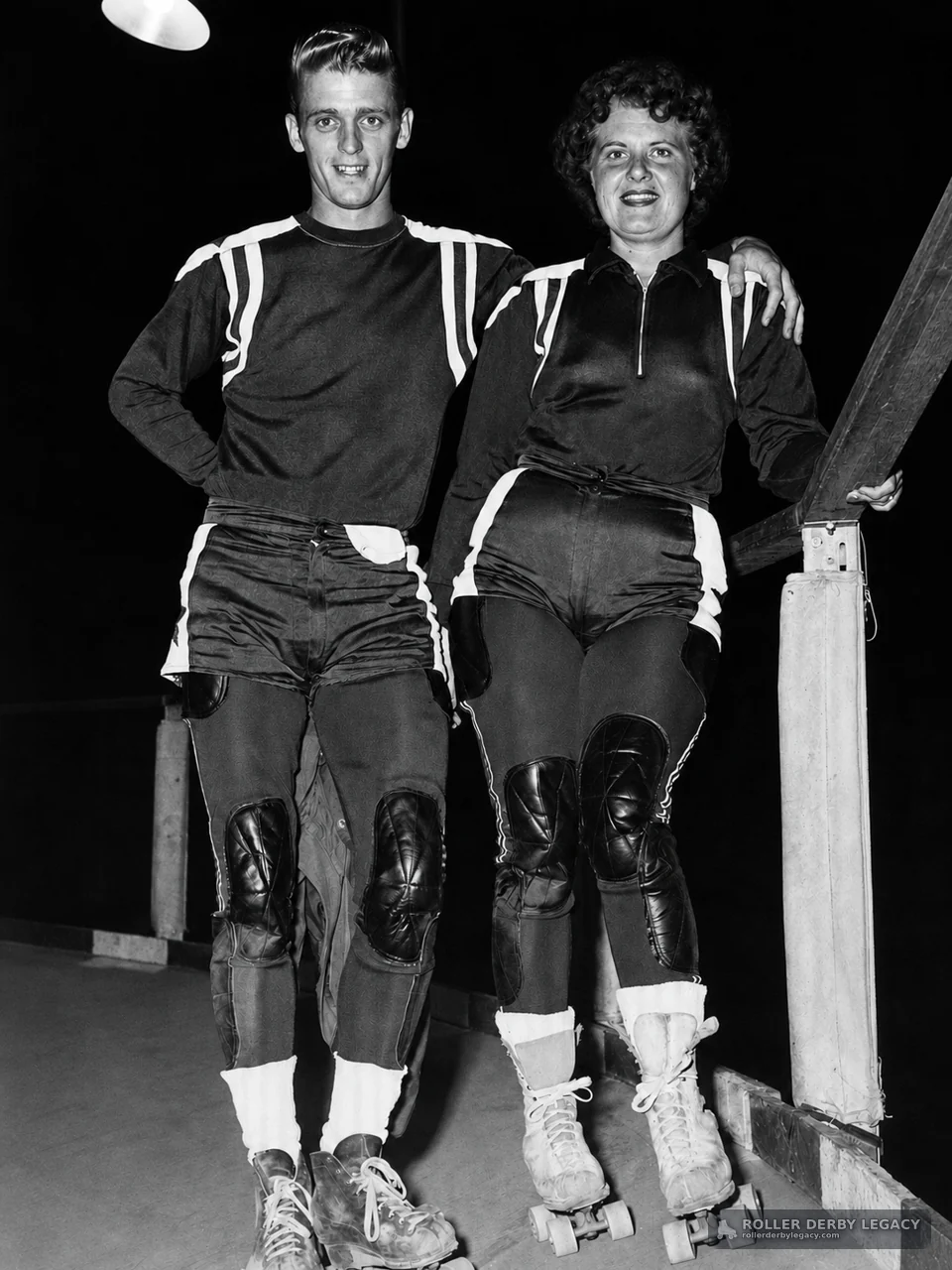 Two Roller Derby Skaters at a Rink Railing