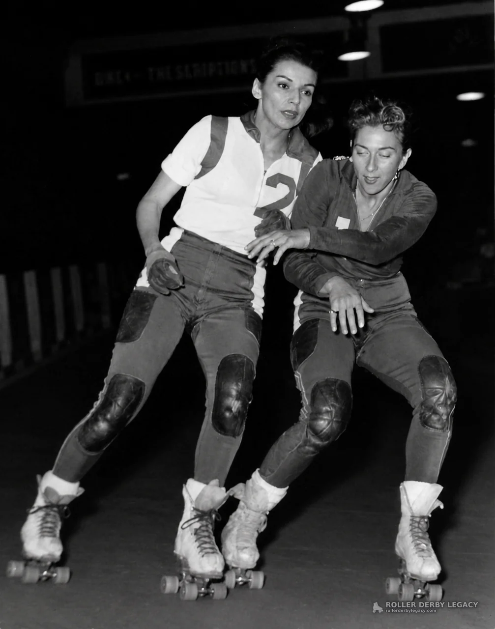 Two Roller Derby Skaters Leaning Into an Indoor Turn