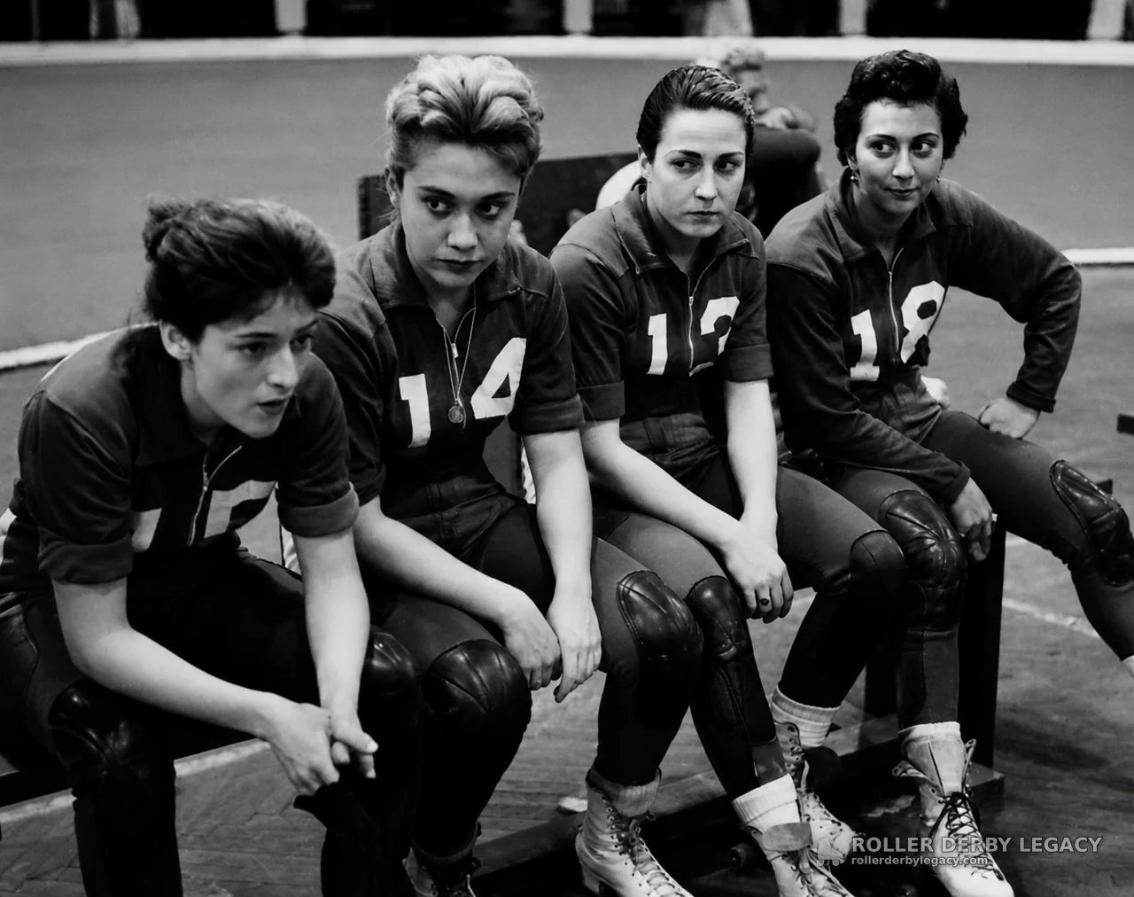 Four Roller Derby Skaters Seated Beside Indoor Track