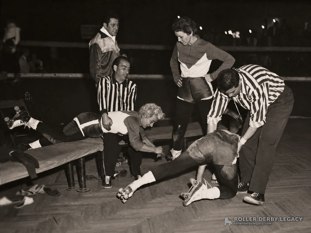 Referees Assist Fallen Skaters Beside Rink Benches