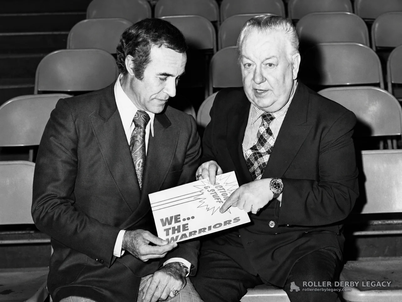 Two Suited Men with “We... The Warriors” Flyer