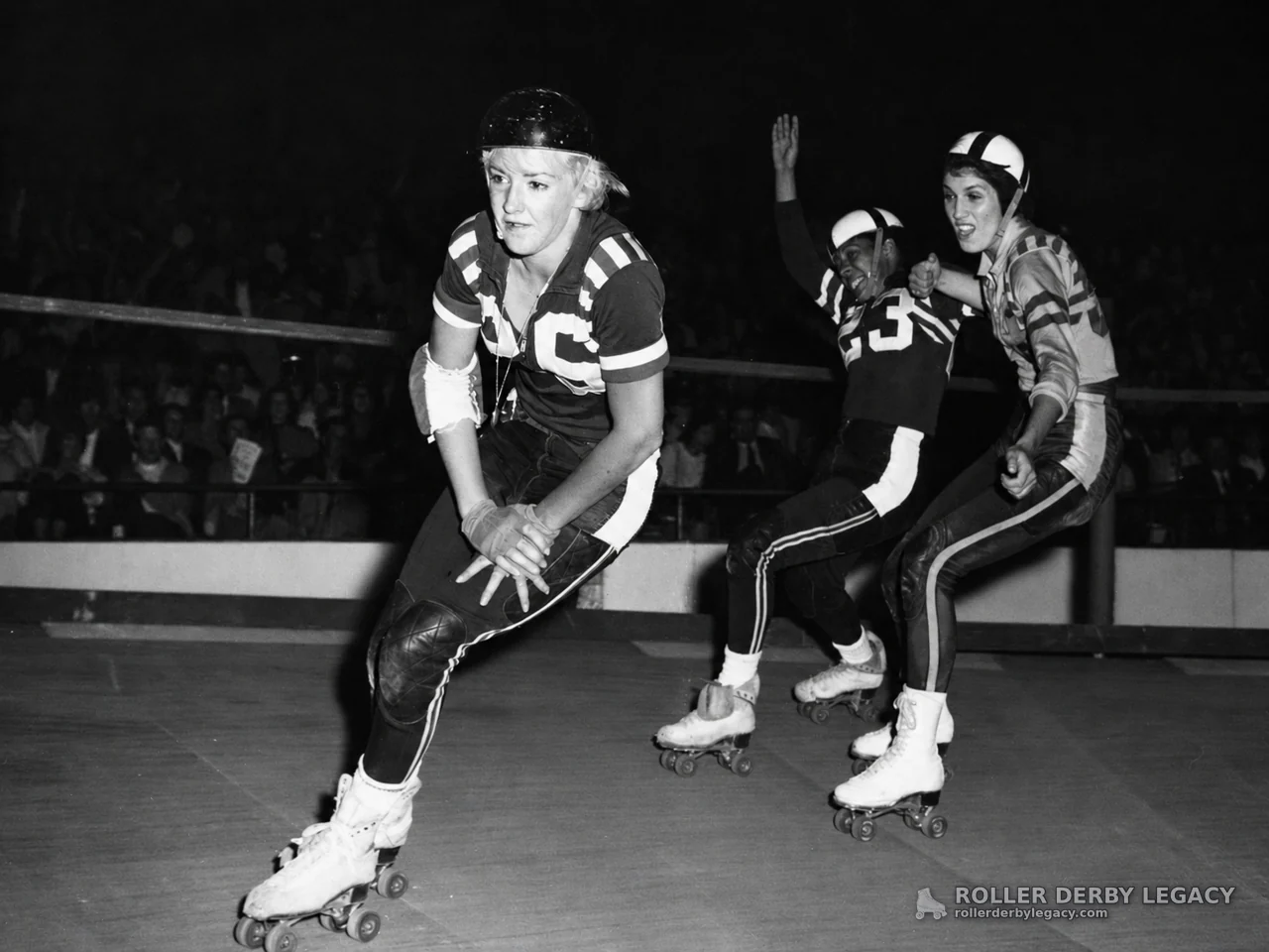 Three Roller Derby Skaters Rounding an Indoor Rink