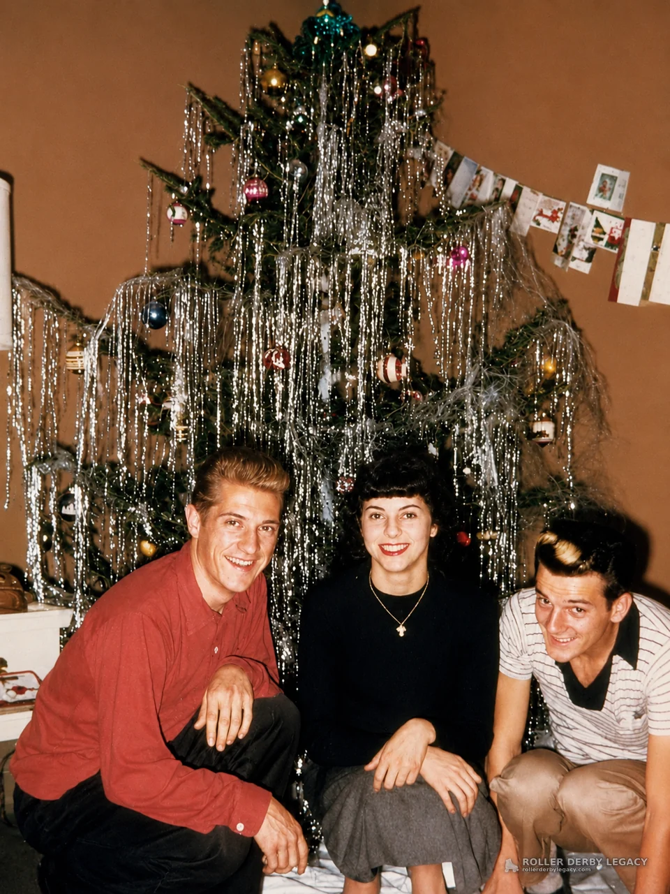 Three People Posing by a Tinsel-Covered Christmas Tree