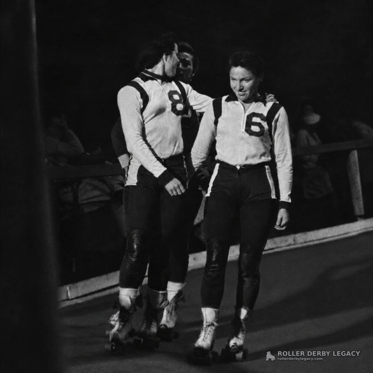Roller Skaters Wearing Numbers 8 and 6 on an Indoor Track