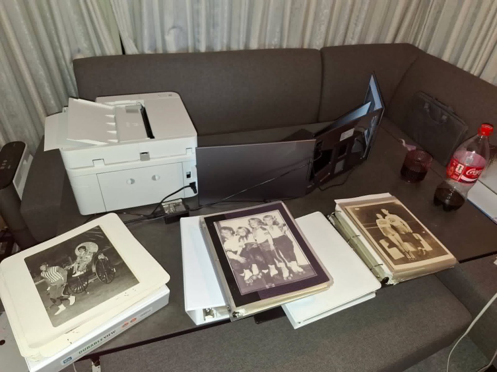A scanning workstation in Japan with a document scanner, monitor, and open binders of historical black-and-white roller derby photographs being digitized.