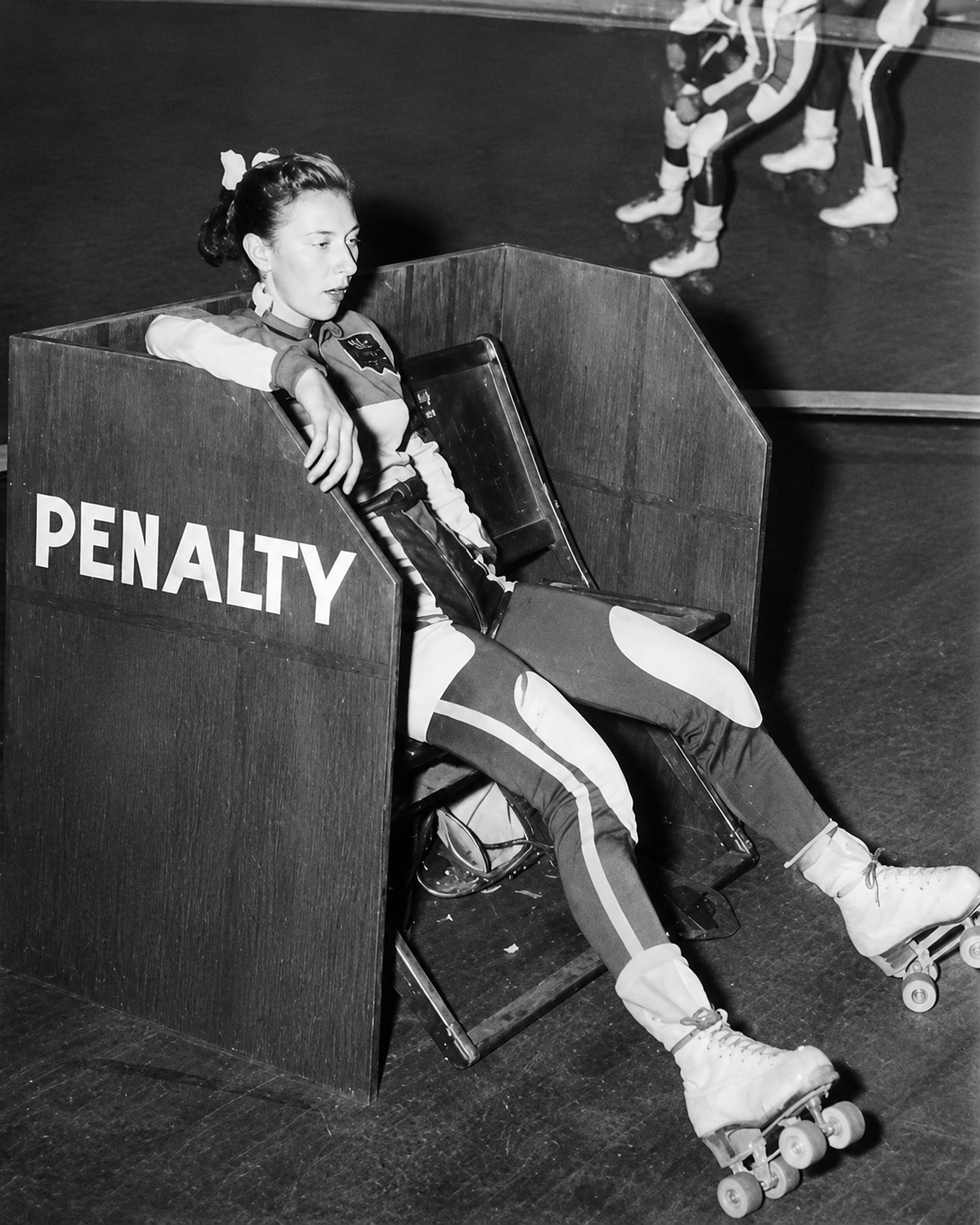 Loretta Behrens seated in the PENALTY box during a roller derby bout.